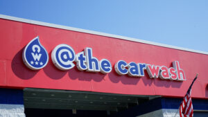 A brightly lit channel letter sign with the words '@ the carwash' in vibrant letters, illuminated on the front of a building.