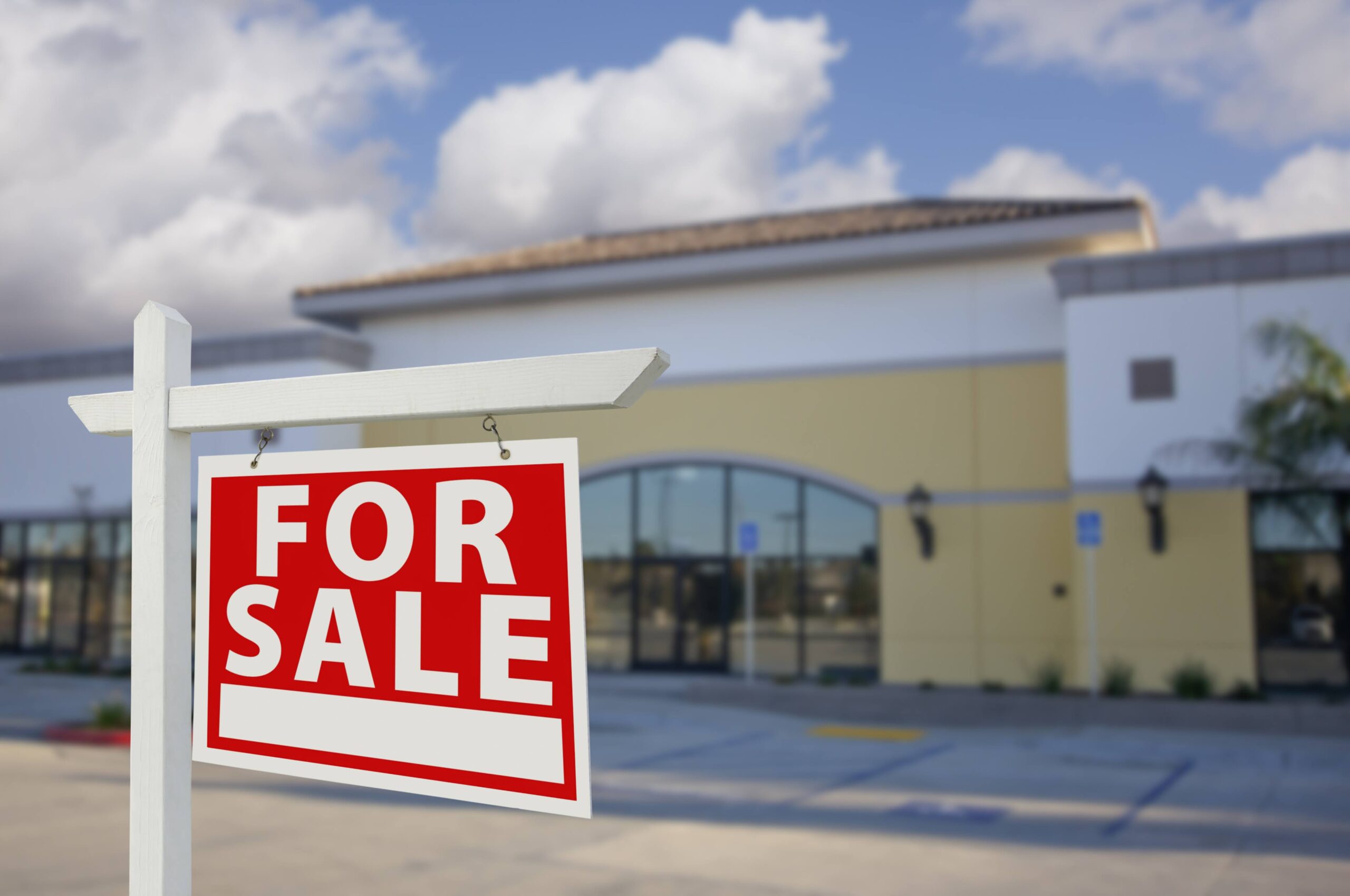 A commercial real estate sign that says "For Sale" in front of a vacant store.