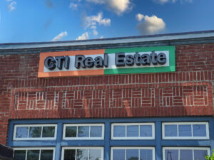 alt="Photo of black real estate channel letter sign affixed to white, orange, and green backer panel in downtown Fredericksburg, Virginia"