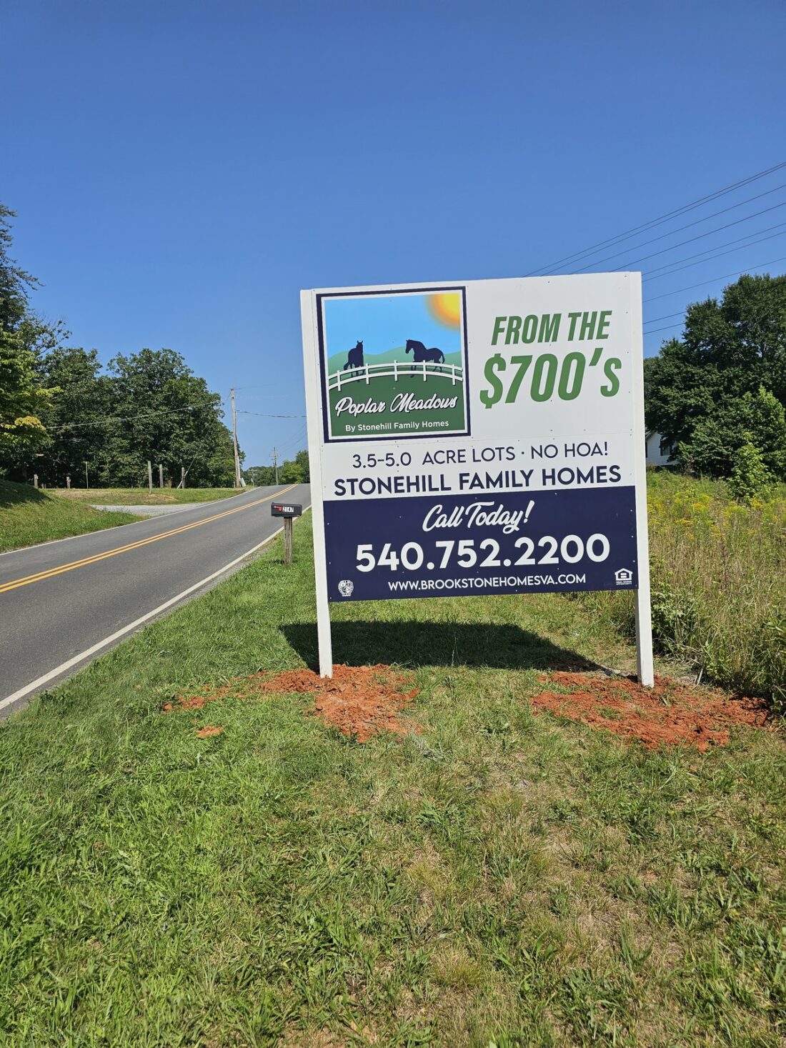 alt="Photo of large vibrant colorful home builder sign in large grassy area off of back road in Stafford, Virginia"