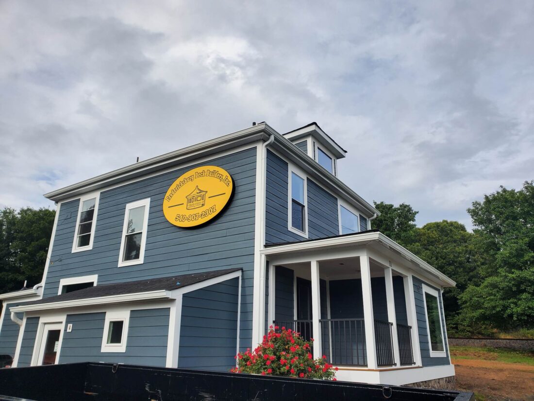 alt="Photo of black and yellow channel letter logo for Fredericksburg Deck Builders mounted to blue house located in Stafford, Virginia"