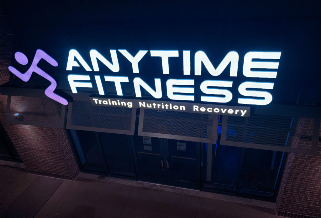 A brilliantly lit Anytime Fitness building sign illuminating the surroundings and standing out in the night.