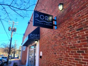 alt="Photo of black and white illuminated blade sign and side view of black and white awning mounted on brick wall in downtown Fredericksburg, Virginia"