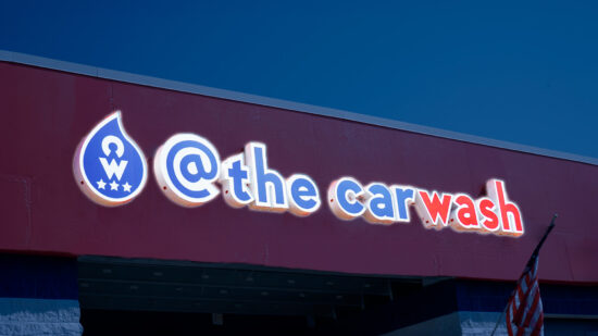 A brightly lit channel letter sign with the words '@ the carwash' in vibrant letters, illuminated on the front of a building.