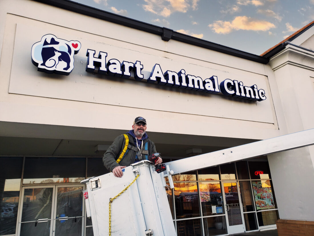 alt="Photo of happy sign installer standing in bucket truck basket after just finishing the Hart Animal Clinic Channel Letter installation located in Fredericksburg, Virginia"