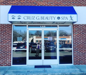 alt="Vibrant photo of blue awning displaying Cruz G. Beauty & Spa on valence located in Fredericksburg, Virginia"