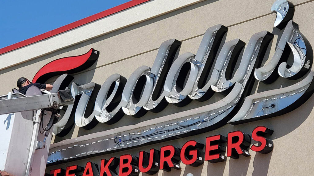 An image of a repair technician fixing the inside of the channel letter sign for Freddy's Steakburgers restaurant.