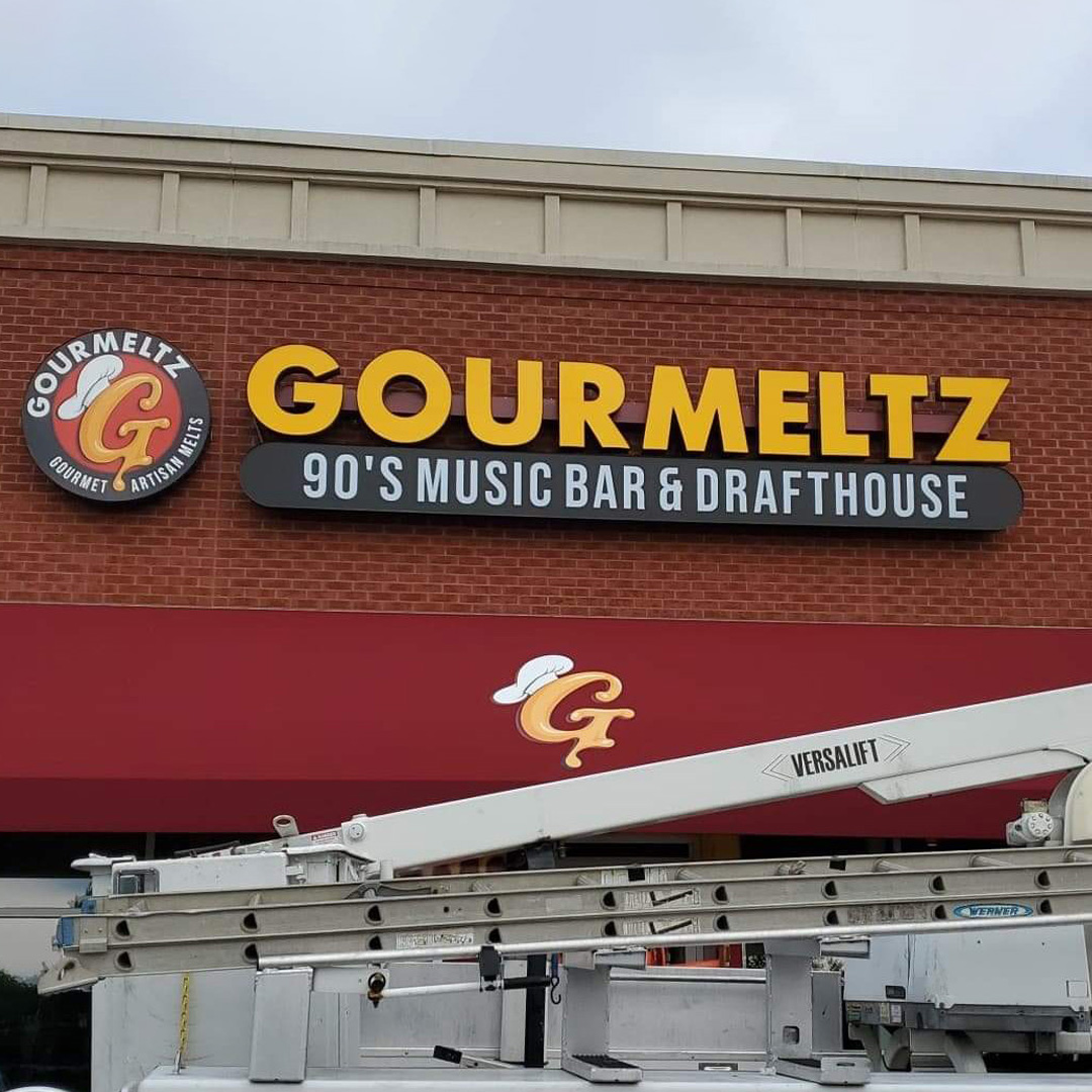A front-facing shot of the Gourmeltz channel letter restaurant sign in Fredericksburg, VA, with a work truck beneath that has just finished installing the sign.