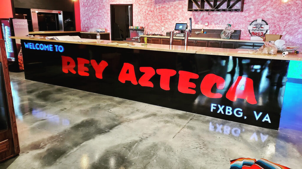 A vinyl graphic that says Rey Azteca, FXBG, VA, installed on the front face of the bar inside the restaurant.