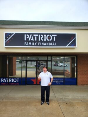 alt="Photo of happy man in front of his brand new PATRIOT FAMILY FINANCIAL illuminated sign cabinet. Sign is American Patriot themed with dark blue, red, and white elements and stars located in Spotsylvania, Virginia"