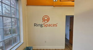 alt="Photo of Black & Orange 3D Acrylic Sign mounted to interior office seating area in Fredericksburg, Virginia"