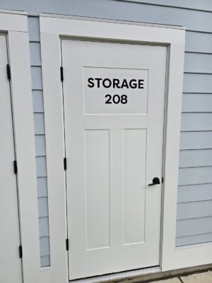 alt="Photo of white storage door with black modern graphics applied stating STORAGE 208 located in Colonial Beach, Virginia"