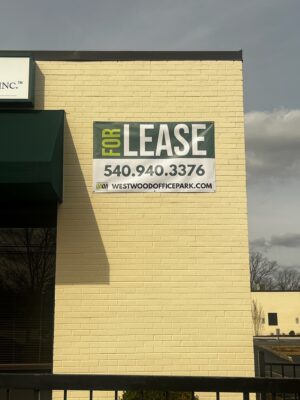 alt="Photo green and white For Lease mounted to yellow brick wall located in Fredericksburg, Virginia"