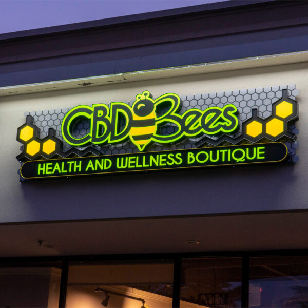 The storefront sign for CBD Bees radiates with bright neon green and yellow hues, set against a dark background, exemplifying high-contrast design for optimal visibility and brand impact.