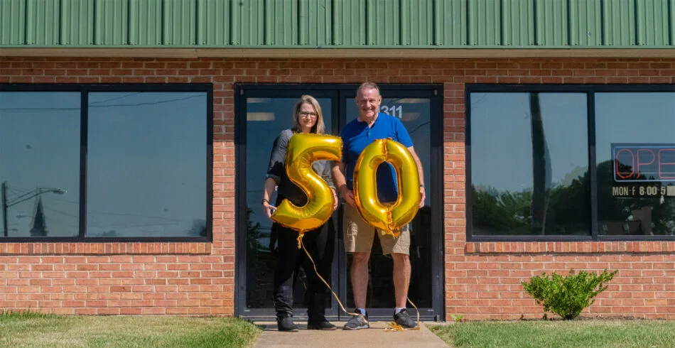 alt="Photo of owners of Distinct Sign Solutions holding gold ballons celebrating 50 years of business located in Fredericksburg, Virginia"