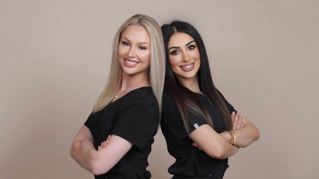 Kaelie Haynie and Mimi Abed, founders of DuoGlo Esthetics in Fredericksburg, VA, smiling and standing back-to-back.