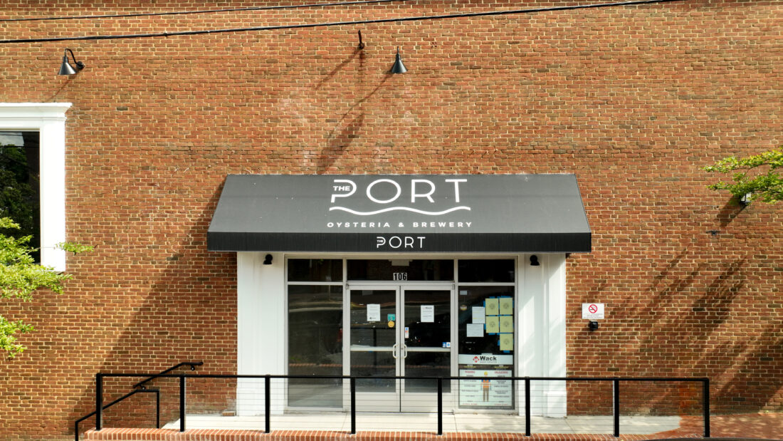 Photo of black fabric awning with white logo graphics for The Port, located in Downtown Fredericksburg, VA. Awning was manufactured & installed by Distinct Sign Solutions in Fredericksburg, VA