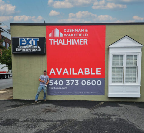 Logo of employee giving thumbs up in front of very large commercial real estate banner in Fredericksburg, VA. Banner was produced & installed by Distinct Sign Solutions in Fredericksburg, VA