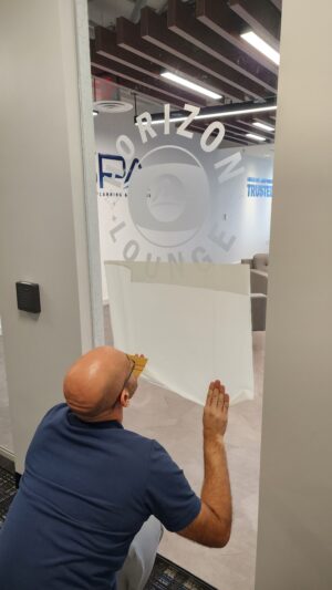 Photo of installer removing last of transfer tape on a frosted vinyl graphic stated Horizon Lounge, located in Alexandria,VA. Graphic was manufactured & installed by Distinct Sign Solutions in Fredericksburg, VA