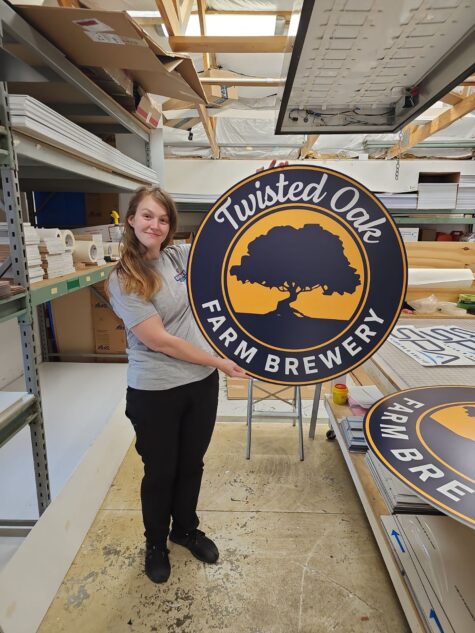 Photo of employee holding custom printed sign for Twisted Oak Brewery. Sign was manufactured by Distinct Sign Solutions