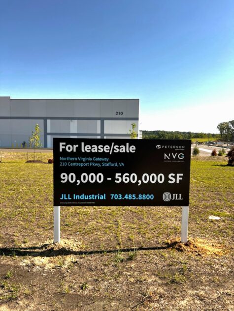 Photo of large black, blue, and white real estate sign in large grassy field in front of massive warehouse. Sign is located in Stafford, VA and was manufactured & installed by Distinct Sign Solutions in Fredericksburg, VA.