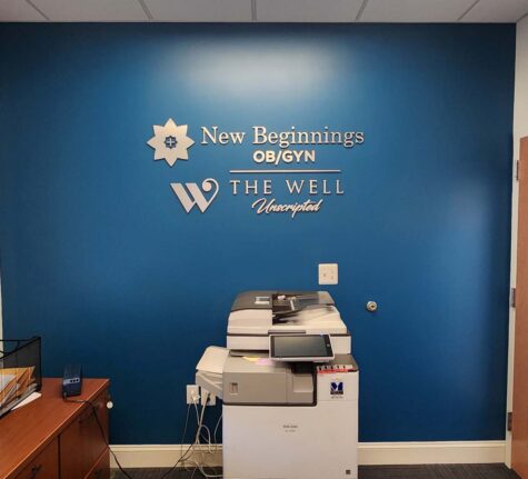 Photo of blue wall with routed brushed aluminum wall sign displaying New Beginnings & The Well Unscripted. Sign is located in Fredericksburg, VA and was manufactured & installed by Distinct Sign Solutions in Fredericksburg, VA