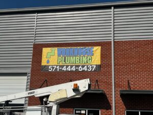 Photo of newly installed bright yellow, green, and blue Workhouse Plumbing banner on brick wall in Stafford VA. Banner manufactured & installed by Distinct Sign Solutions in Fredericksburg, VA