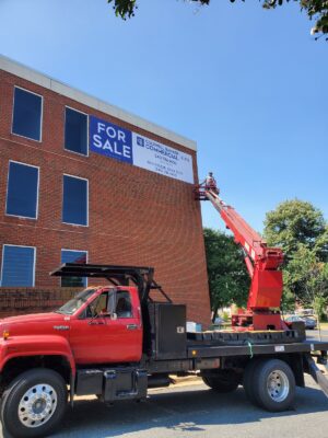 Photo of large bucket truck installing large banner in Fredericksburg, VA. Banner was manufactured & installed by Distinct Sign Solutions in Fredericksburg, VA