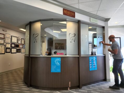 Photo of installer doing finishing touches on frosted vinyl on receptionist desk glass panes in Fredericksburg, VA. Graphics were manufactured & installed by Distinct Sign Solutions in Fredericksburg, VA