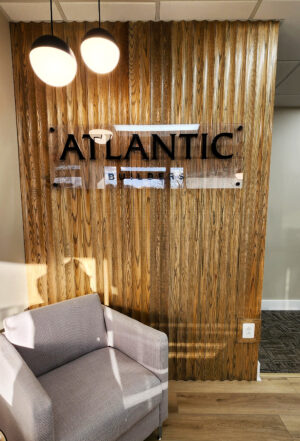 Photo of office entrance area wooden textured wall with acrylic wall sign. Sign is black routed acrylic mounted to a clear backer panel and installed with standoffs. Sign was manufactured & installed by Distinct Sign Solutions in Fredericksburg, VA