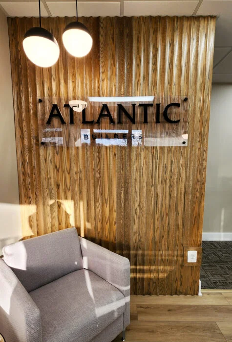 Photo of office entrance area wooden textured wall with acrylic wall sign. Sign is black routed acrylic mounted to a clear backer panel and installed with standoffs. Sign was manufactured & installed by Distinct Sign Solutions in Fredericksburg, VA