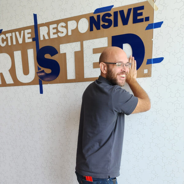 A smiling technician aligns and presses large vinyl letters onto an interior wall, adding a professional, branded finish to the space.