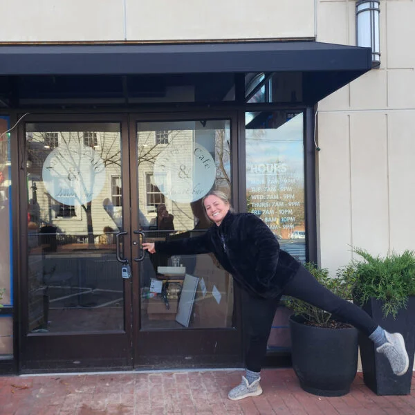 Owner, Anita, posing at the front entrance of Anita’s Cafe & Dessert Bar in Downtown Fredericksburg, featuring stylish vinyl graphics and an inviting awning created by Distinct Sign Solutions in Fredericksburg, VA.