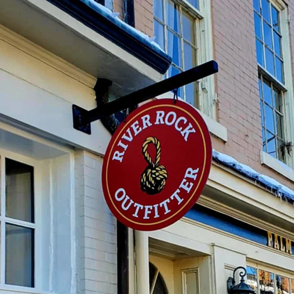 Striking hanging blade sign for River Rock Outfitter in Downtown Fredericksburg, designed with bold red and gold accents by Distinct Sign Solutions in Fredericksburg, VA, to reflect the store’s adventurous spirit.