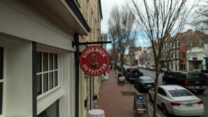 Photo of red blade sign for River Rock outfitter on steel black bracket. Sign is hanging on side of building in Downtown Fredericksburg, VA. Sign was manufactured & installed by Distinct Sign Solutions in Fredericksburg, VA