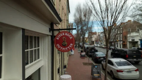 Photo of red blade sign for River Rock outfitter on steel black bracket. Sign is hanging on side of building in Downtown Fredericksburg, VA. Sign was manufactured & installed by Distinct Sign Solutions in Fredericksburg, VA