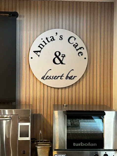 Photo of cream & black acrylic wall sign on wooden slat wall in Downtown Fredericksburg, VA cafe. Sign was manufactured & installed by Distinct Sign Solutions in Fredericksburg, VA