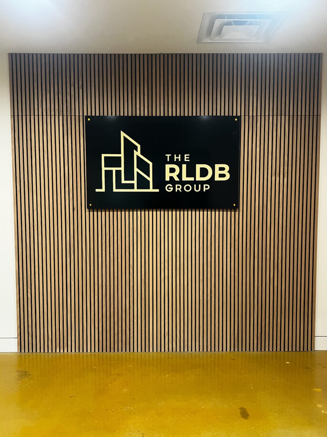 Photo of black and gold acrylic wall sign mounted to wooden slat wall in Stafford, VA contractor's office. Sign was manufactured & installed by Distinct Sign Solutions in Fredericksburg, VA