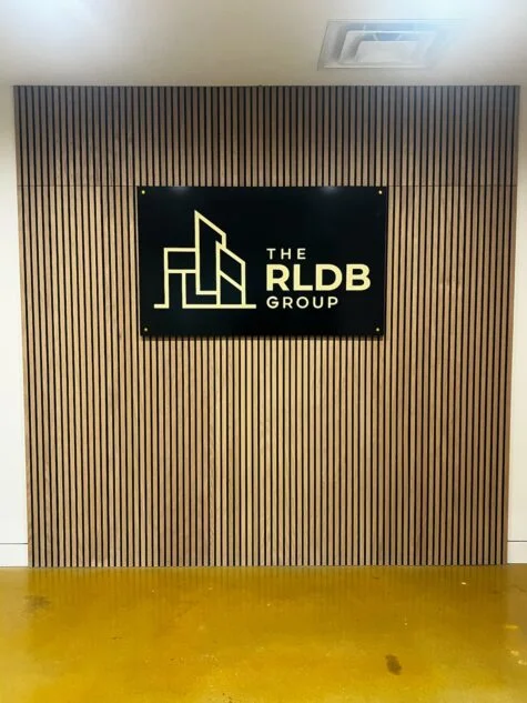 Photo of black and gold acrylic wall sign mounted to wooden slat wall in Stafford, VA contractor's office. Sign was manufactured & installed by Distinct Sign Solutions in Fredericksburg, VA