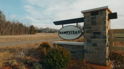 Photo of custom stone entrance monument with Hampstead blade sign affixed to wooden pole in Stafford, VA. Sign was manufactured & installed by Distinct Sign Solutions in Fredericksburg, VA