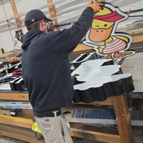 Distinct Sign Solutions team assembling a Duck Donuts character sign in Fredericksburg, VA