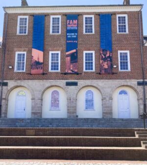 Photo of large vertical banners affixed to brick building in Market Square in Downtown Fredericksburg for the Fredericksburg Area Museum. Banners were manufactured & installed by Distinct Sign Solutions in Fredericksburg,VA