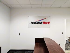 Photo of Paradigm Max Q Acrylic Wall sign mounted to white receptionist wall in Stafford, VA. Sign was manufactured & installed by Distinct Sign Solutions in Fredericksburg, VA