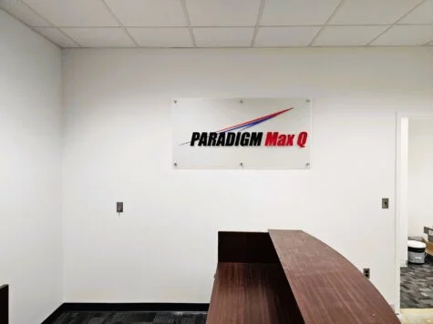 Photo of Paradigm Max Q Acrylic Wall sign mounted to white receptionist wall in Stafford, VA. Sign was manufactured & installed by Distinct Sign Solutions in Fredericksburg, VA