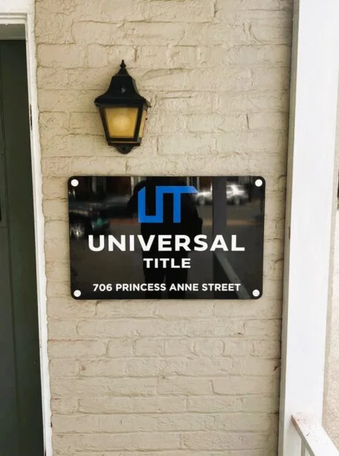 Photo of black, blue, and white custom routed sign set with brushed metal standoffs mounted to brick wall in Fredericksburg, VA. Sign was manufactured & installed by Distinct Sign Solutions in Fredericksburg, VA