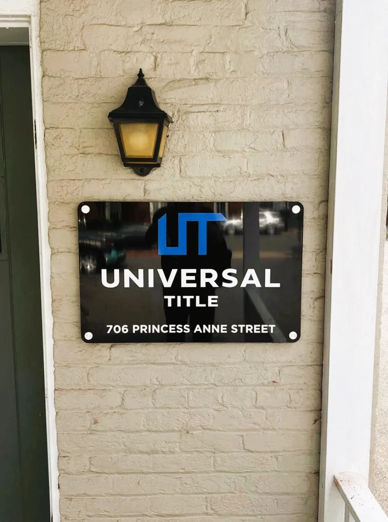 Photo of black, blue, and white custom routed sign set with brushed metal standoffs mounted to brick wall in Fredericksburg, VA. Sign was manufactured & installed by Distinct Sign Solutions in Fredericksburg, VA