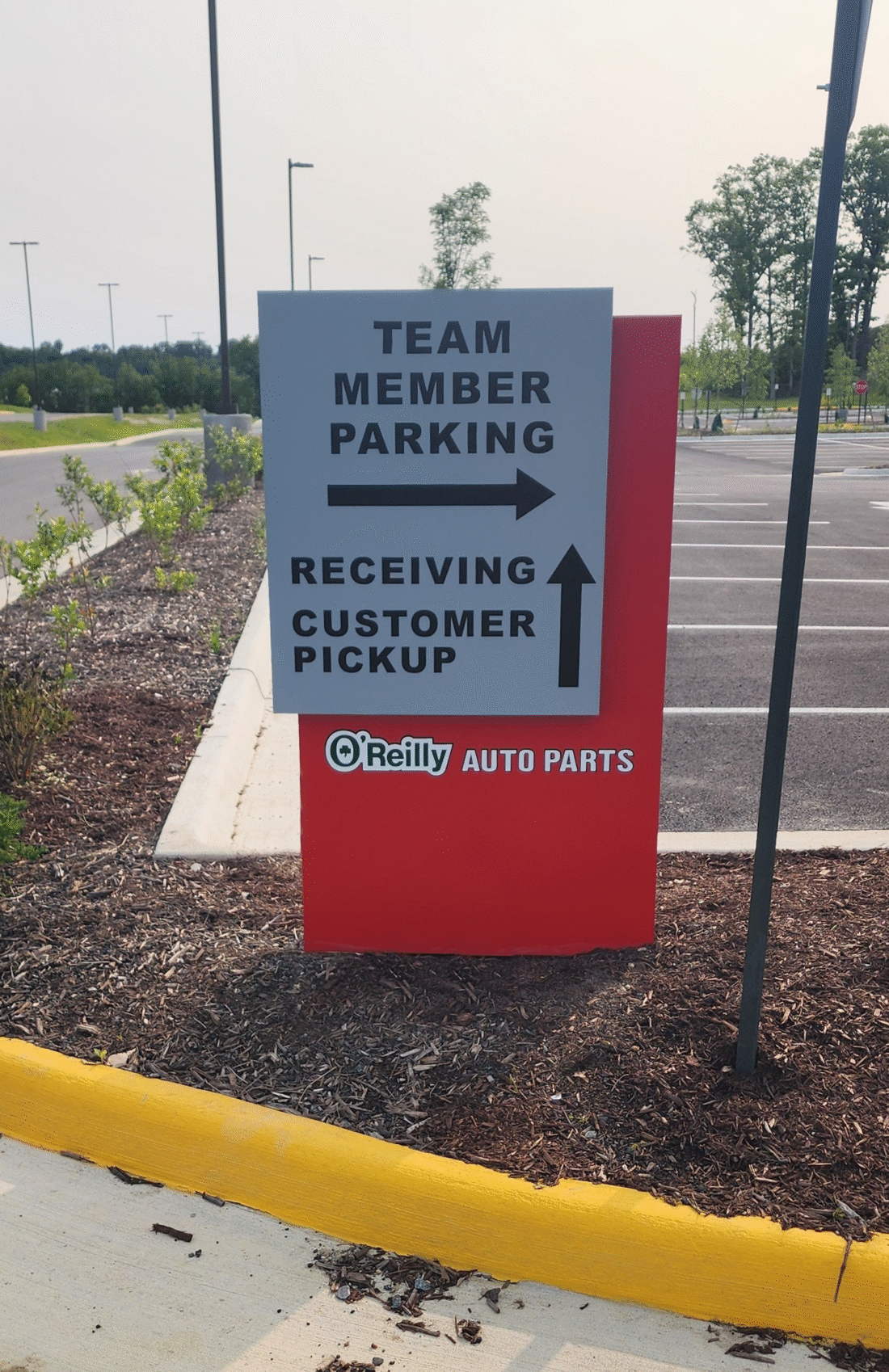 Photo of gray and red O'Reilly Aut Parts post sign in mulch bed at Stafford, VA property. Sign was installed by Distinct Sign Solutions in Fredericksburg, VA