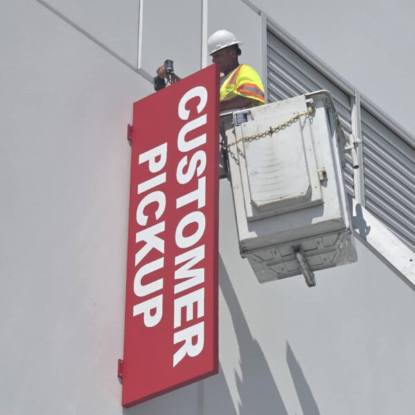 Sign installer mounting red “Customer Pickup” sign on the exterior wall of a distribution facility