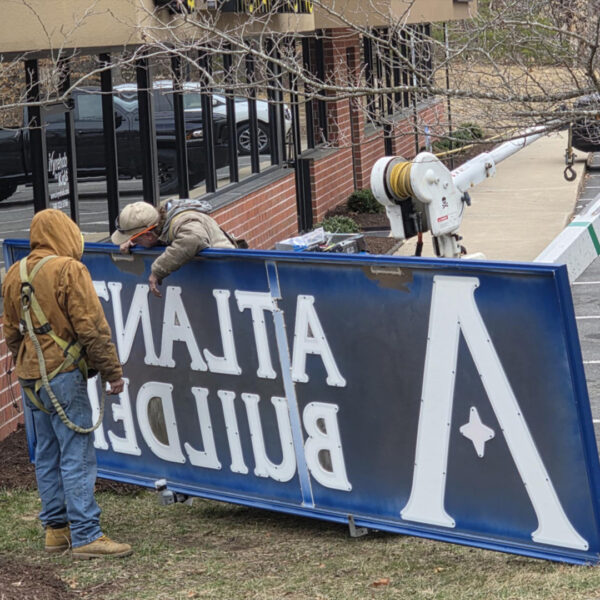 Technicians inspecting cabinet sign face and wiring on ground prior to lift install at Atlantic Builders.