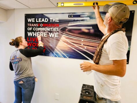 Photo of two installers doing finishing touches on interior acrylic wall sign in Fredericksburg, VA. Sign was manufactured & installed by Distinct Sign Solutions in Fredericksburg, VA